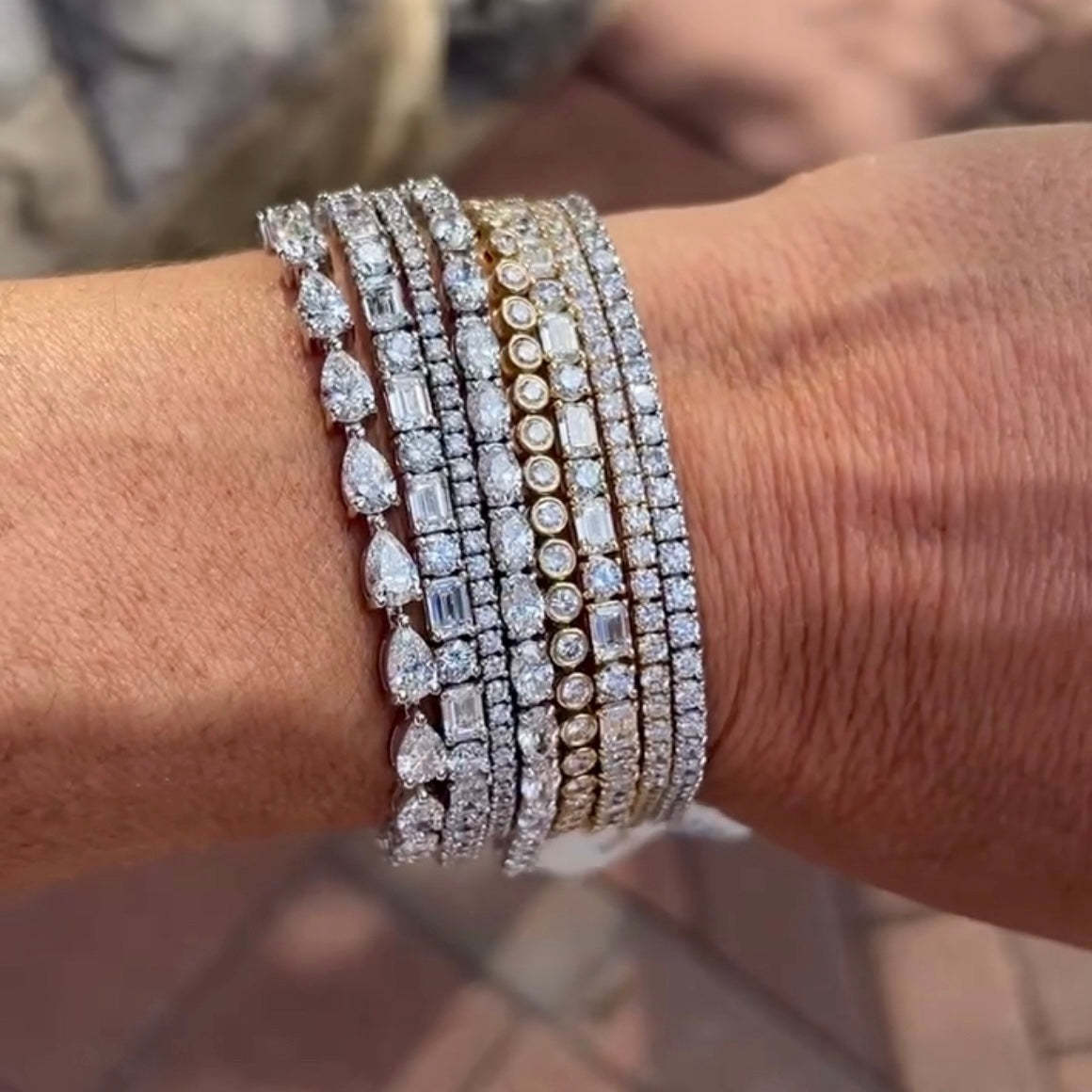 Stack of eight lab diamond tennis bracelets in an assortment of styles on a woman's wrist.